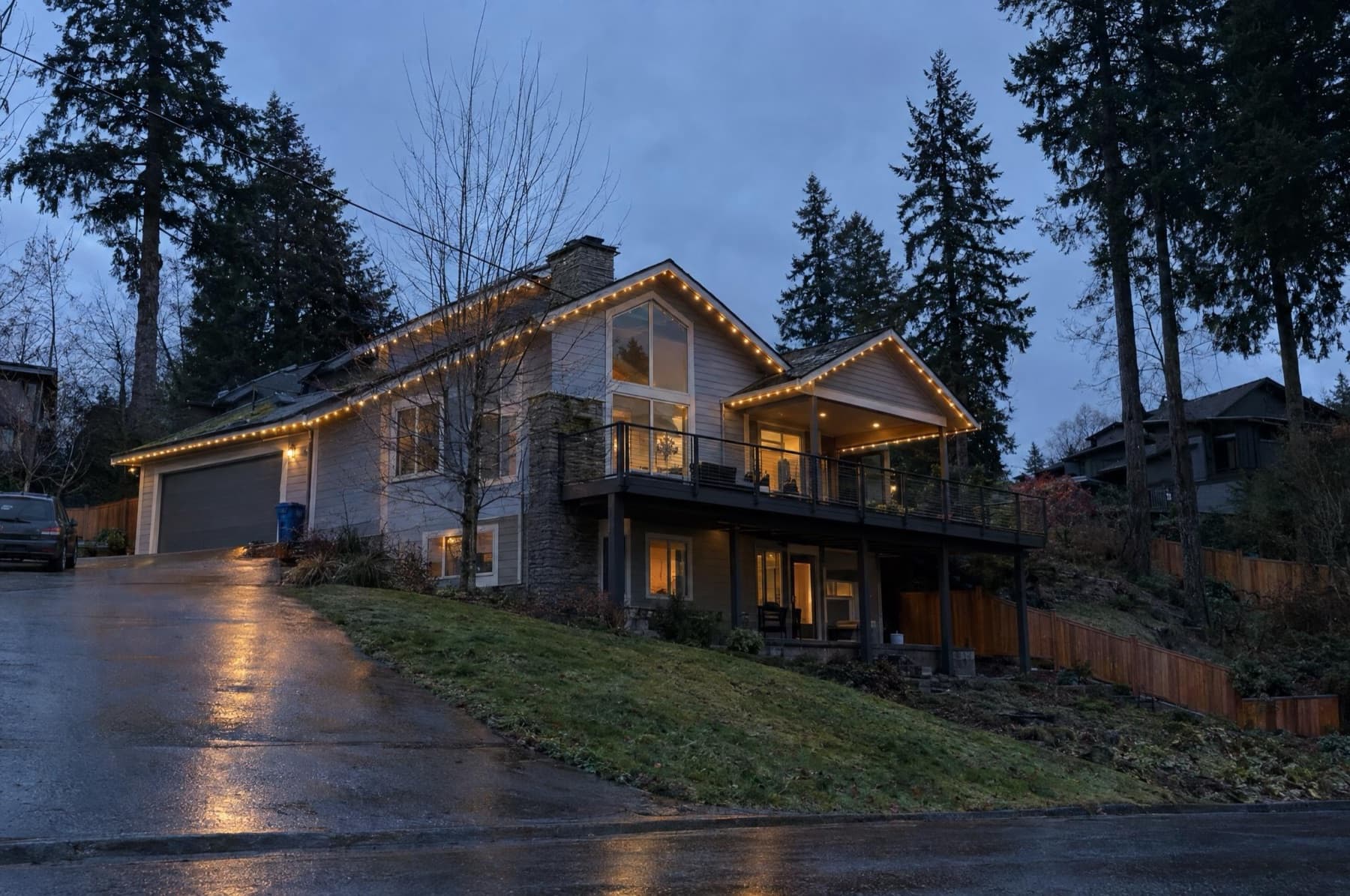 Hillside home seen from below with the roofline and deck edge lit warm white