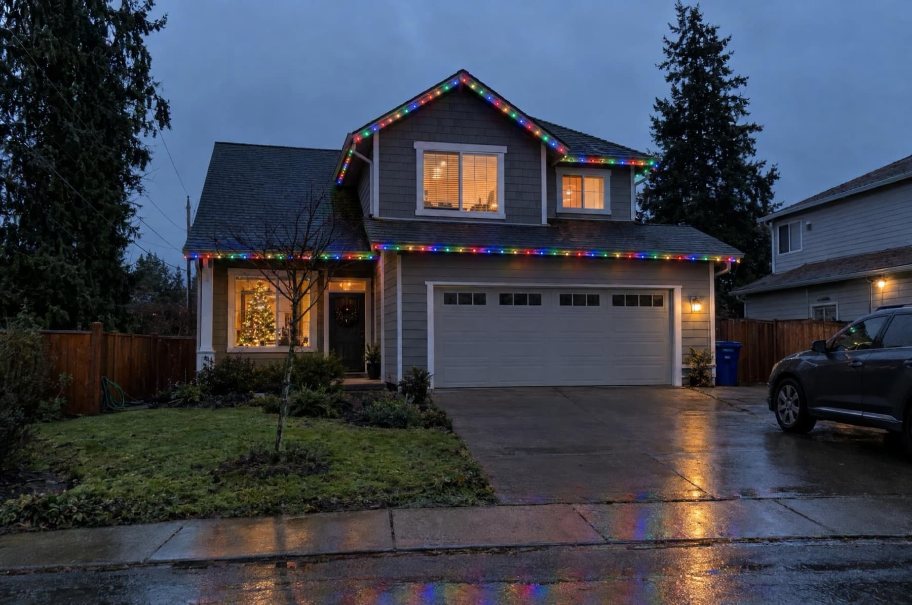 Two-story home with multicolor roofline lights and a lit tree in the window