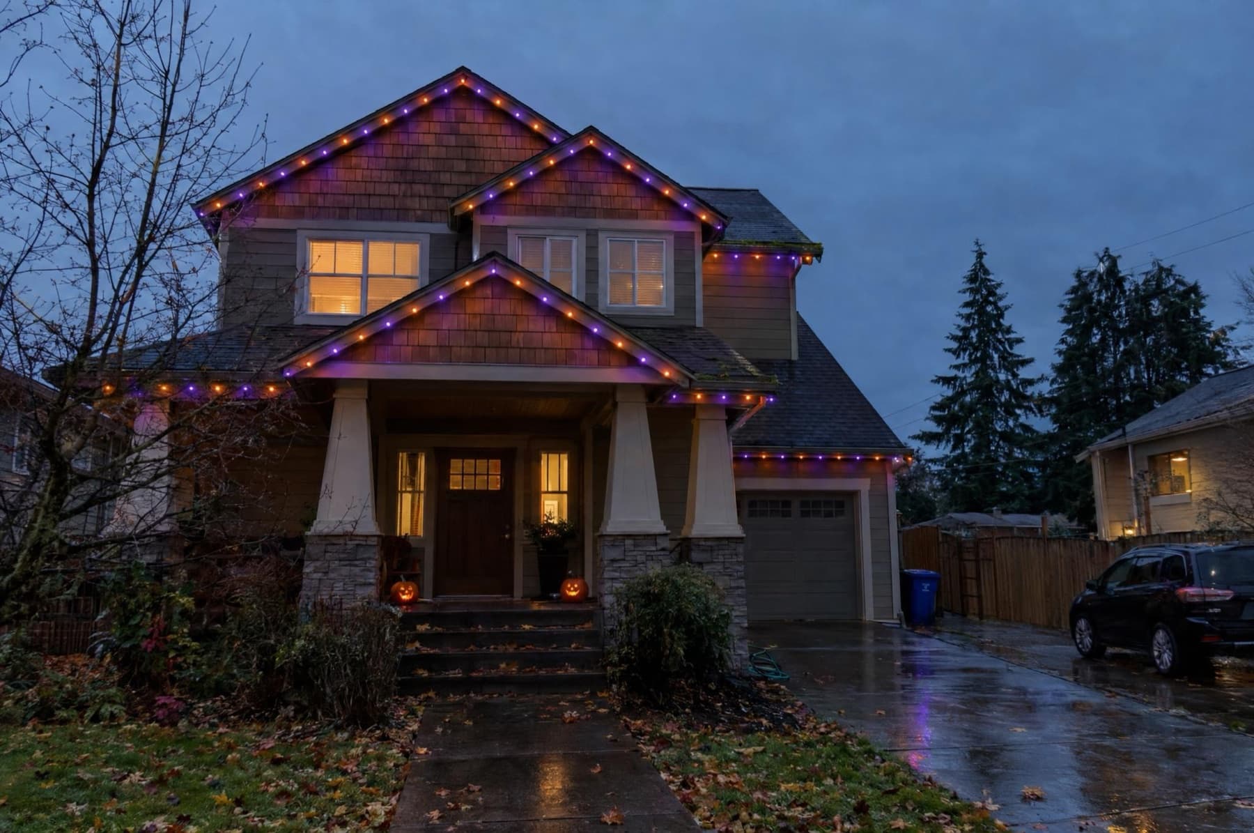 Craftsman home with orange and purple roofline lights, pumpkins on the porch