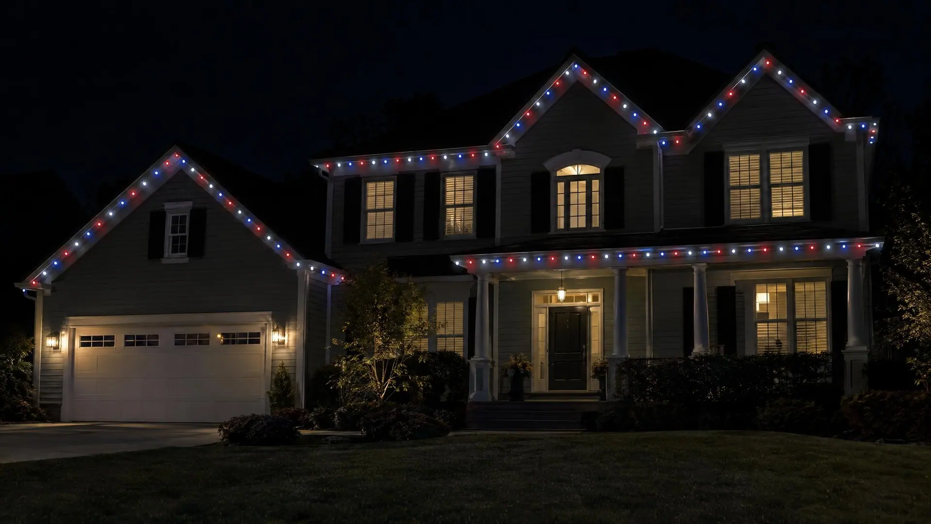 A colonial home at night with red, white and blue roofline lights