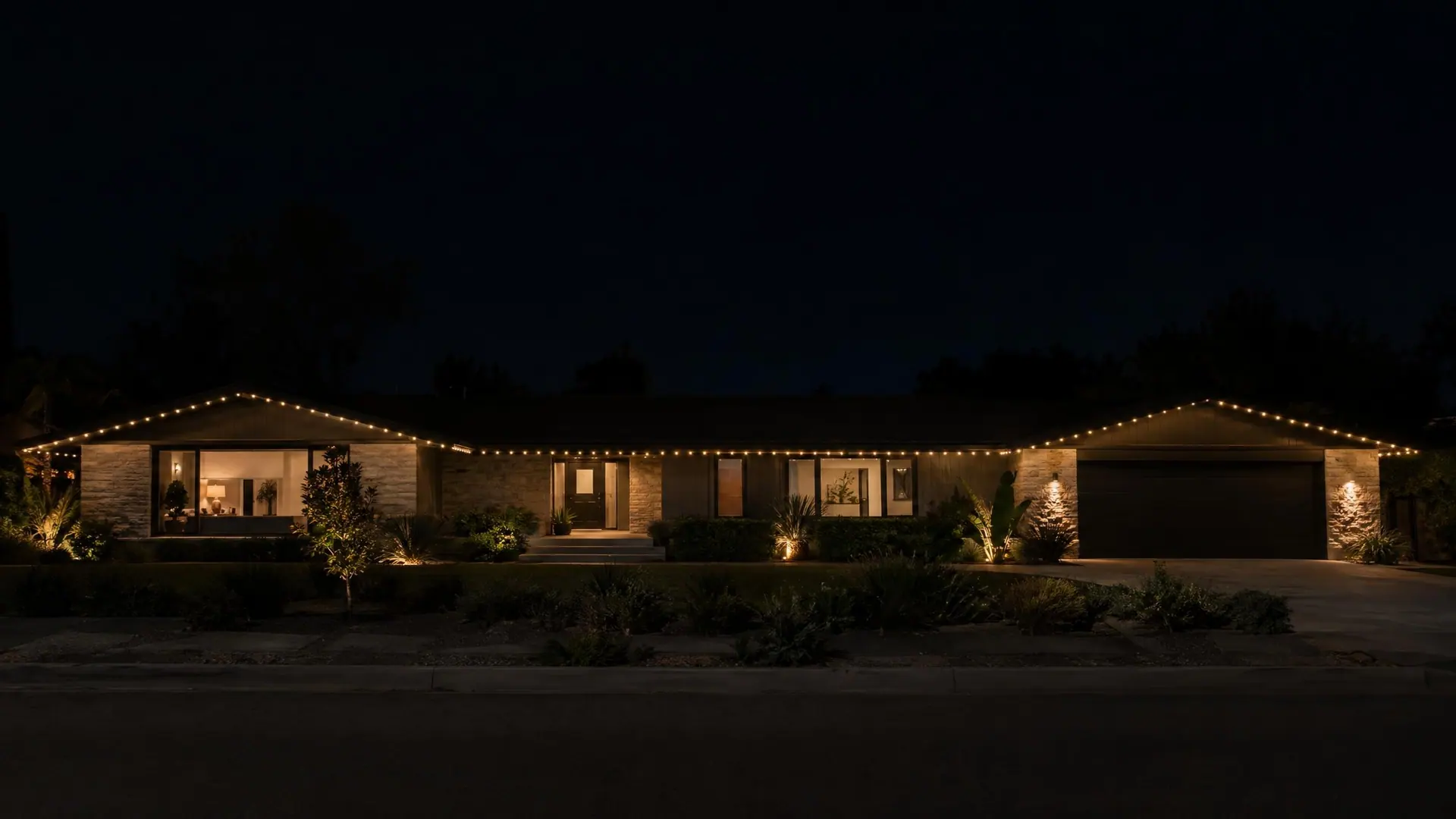 A long single-story rambler at night with warm-white permanent roofline lighting